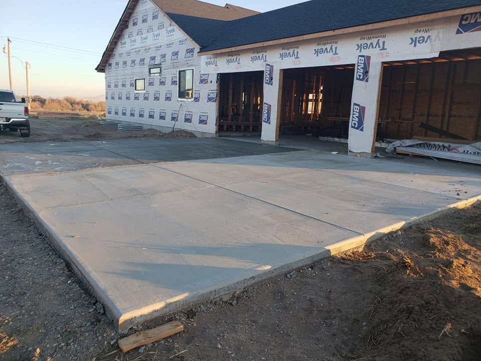 New custom home under construction with fresh concrete driveway and three-car garage