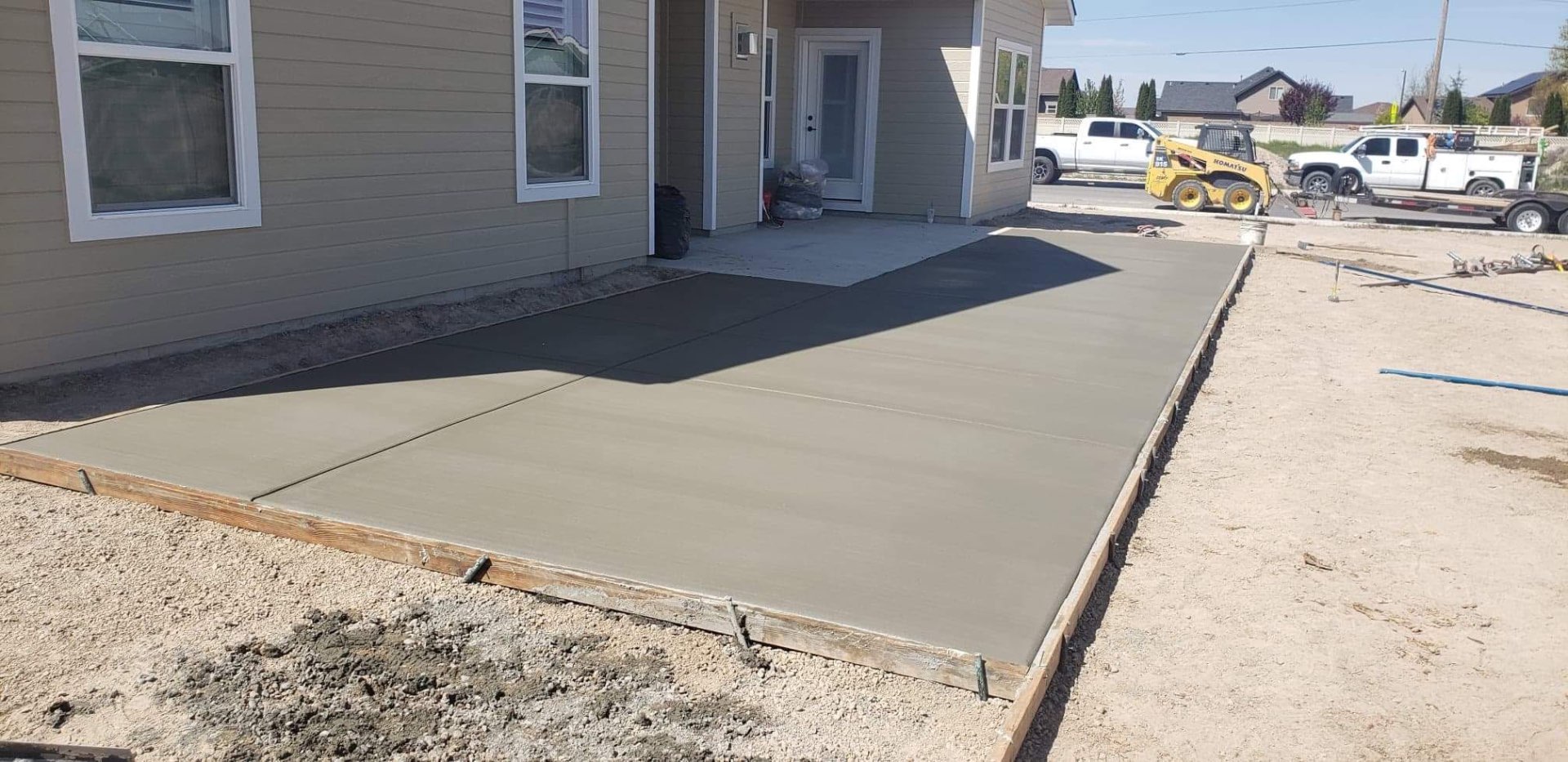 Freshly poured broom-finish concrete walkway and pad extending along the side of a home